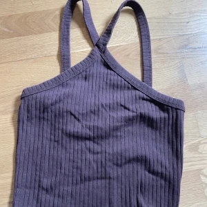 Brun ribbad linnetopp från Gina Tricot - Säljer en brun ribbad linnetopp från Gina Tricot med smala axelband som korsas framtill. Toppen är ärmlös och har en croppad passform, perfekt för varma dagar.