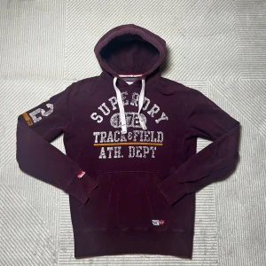 Vinröd Superdry hoodie | S - Superdry track and field hoodie | defekter förekommer (Se bild) men har fortfarande mycket kvar att ge | frågor? Hör då av dig | ⚜️