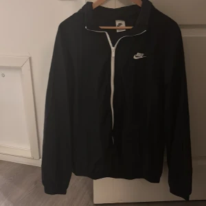 Svart vindjacka från Nike - Hejsa!! Säljer en svart vindjacka från Nike med vit dragkedja och logga på bröstet. Jackan har huva och långa ärmar, perfekt för blåsiga dagar. Enkel och stilren design som passar till det mesta. Har inte tagit på mig så mycket. Priset kan diskuteras👍