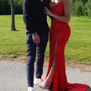 Röd långklänning med slits - Säljer en snygg röd långklänning med figurnära passform och hög slits framtill. Klänningen har smala axelband och en elegant, något glansig finish. Perfekt för bal eller festkväll! Använd endast en gång!