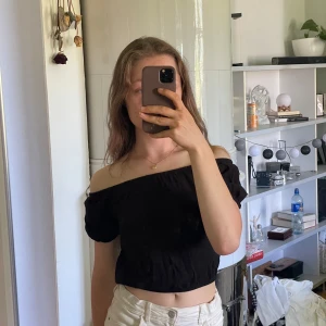 Svart offshoulder topp från H&M - Säljer en svart offshoulder topp från H&M med korta puffärmar och croppad passform. Toppen har en elastisk kant upptill och nertill som ger en snygg siluett. Perfekt till sommaren!