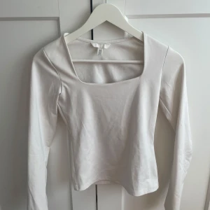 Vit långärmad topp med fyrkantig ringning - Säljer en stilren vit långärmad topp från H&M med snygg fyrkantig ringning. Toppen är i mjuk bomull och passar perfekt till jeans eller kjol. Enkel och clean look som är lätt att matcha.
