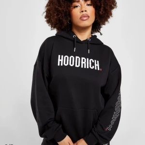 Svart hoodie från Hoodrich - Säljer en svart hoodie från Hoodrich med vit logga framtill och tryck på ryggen. Hoodien har huva med dragsko, magficka och tryck även på ena ärmen. Perfekt för en avslappnad streetwear-look.