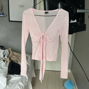 Ljusrosa omlottopp från Gina Tricot - Supersöt ljusrosa omlottopp från Gina Tricot med långa ärmar och knyt framtill. Tunn och mjuk i materialet, perfekt för lager på lager eller som den är. Djup v-ringning och croppad passform ger en trendig look.