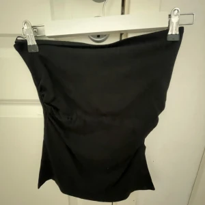 Svart tubtopp - En stilren svart bandeau tubtopp med enkel design. Toppen är axelbandslös och har en tight passform som sitter snyggt mot kroppen. Perfekt att matcha med jeans eller kjol för en trendig look.