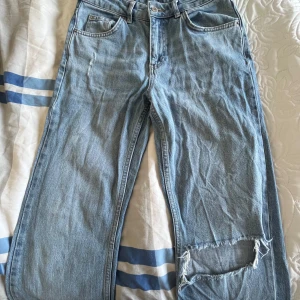 Blå jeans från Gina Tricot - Snygga blå jeans från Gina Tricot med en avslappnad passform. De har en cool reva på ena benet och klassisk femficksdesign. Perfekta för en casual look.
