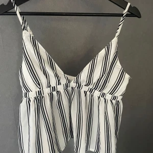 Randig vit och svart topp - Säljer en snygg vit och svart randig topp med smala axelband och v-ringning från Bikbok. Jättefin till sommaren, använd en gång. 💞