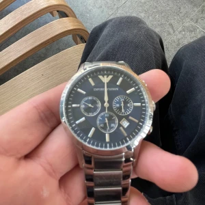 Silverfärgad klocka från Emporio Armani - Snygg klocka från Emporio Armani med en stilren svart urtavla och silverfärgad boett. Batteri är dött. Dm vid frågor