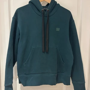 Acne Studios Ferris face hoodie Grön - Grön hoodie i bomull med Acnes signaturmärke. Klassisk, stilren hoodie med justerbar luva. Mycket fin grön färg. Unisex, passar både män och kvinnor.  Superbra skick, inga skavanker eller tecken på användning.  Nypris: 2000-4000kr.   Skick: Mycket gott, 8/10.  Storlek: M 175/96A (passar även S) Färg: Bottle Green Material: 100% bomull  Rök- och djurfritt hem.   Längd (topp till botten): 60 cm  Bredd (armhåla till armhåla): 57 cm Armlängd (från armhålan): 45 cm 