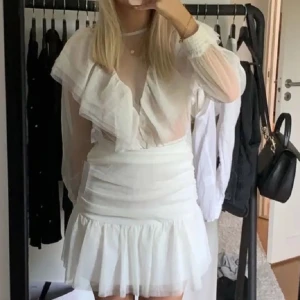 Vit klänning med volangdetaljer - Elegant vit klänning med volangdetaljer och långärmad design. Klänningen har en v-ringad stil och en kort längd som ger en chic look. Perfekt för sommarens festligheter. det är en kjol och en topp men ser ut som en klänning!🥰