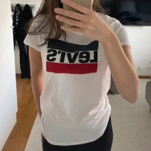 Vit Levi’s t-shirt - Vit Levi’s t-shirt med tryck i strö M. Använd fåtalet gånger. Ena lappen i nacken börjar lossna lite men inget som förstör tröjans söm