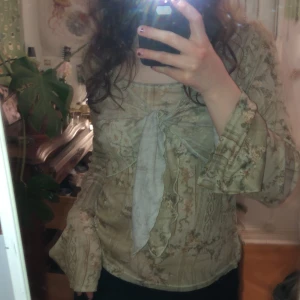 Beige blommig topp från Evy by Bobo - Säljer en beige blommig topp från Evy by Bobo. Toppen har långa ärmar och en knytning framtill som ger en fin detalj. Perfekt för en bohemisk look.