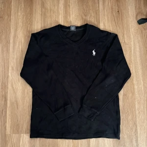 Svart tröja från Polo Ralph Lauren - Säljer en stilren svart tröja från Polo Ralph Lauren med v-ringning och det klassiska logotypbroderiet på bröstet. Tröjan har långa ärmar och är perfekt för en avslappnad men elegant look.