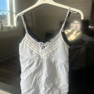 Sommar topp  - Säljer en söt blå- och vitrandig linnetopp med smala axelband och v-ringning. Toppen har en smockdetalj på ryggen för bättre passform. 