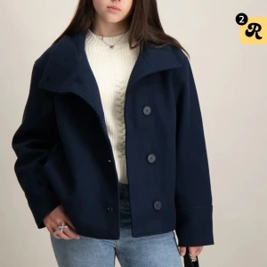 Mörkblå kappa med knappar - Snygg mörkblå kappa med stora knappar framtill. Jackan har en klassisk krage och långa ärmar, perfekt för kyligare dagar. Den har en stilren och tidlös design som passar till många olika outfits. Har knappt använts 