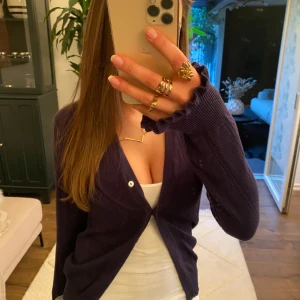 Mörkblå kofta med knappar - Säljer en stilren mörkblå (ser lila ut på bilden) kofta med knappar framtill. Koftan har långa ärmar och en djup v-ringning, perfekt för lager-på-lager-stil. Passar både till vardags och mer uppklädda tillfällen.