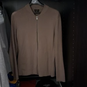 Brun tröja med dragkedja från Massimo Dutti - Säljer en stilren brun/beige tröja från Massimo Dutti i bomull. Tröjan har en dragkedja framtill och långa ärmar, perfekt för en elegant och avslappnad look. Tröjan är i bra skick utan defekter. Skriv för funderingar. Pris kan diskuteras