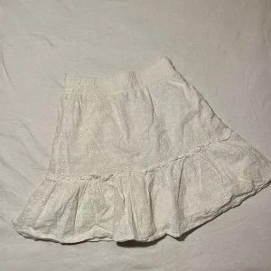 Vit kjol med volang - Säljer denna söta vita kjol med volangdetaljer och broderade. Elastisk midja för bekväm passform. Pris kan diskuteras!