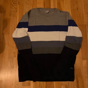 Randig tröja från WeSC - Säljer en snygg randig tröja från WeSC i storlek medium. Tröjan har breda ränder i grått, blått, vitt och svart. Perfekt för en avslappnad stil.
