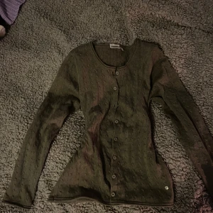 Grön kofta med knappar - Säljer en stilren grön kofta med knappar framtill. Den har en rund halsringning och långa ärmar, perfekt för lager på lager-stil. Passar bra till både vardag och mer uppklädda tillfällen.