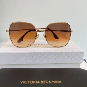 Solglasögon Victoria Beckham - Snygga solglasögon från Victoria Beckham med fyrkantiga glas och en elegant guldfärgad ram. Glasen har en brun toning som ger en stilren look. Perfekta för soliga dagar! Nypris 3000kr smartbyglasses.se 
