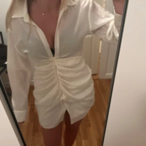 Vit klänning från Zara - Säljer en stilren vit klänning från Zara med långärmad design och knytning framtill. Perfekt för en elegant look. Klänningen har en kort längd och en klassisk krage.