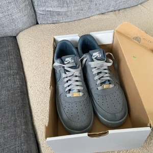 Grå Nike Air Force sneakers - Snygga grå Nike Air Force sneakers med klassisk design och vit sula. Skorna har snörning och är perfekta för en stilren look. De är förpackade i originalkartong. Använt 2 gånger de passade inte 