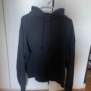Svart hoodie med ficka - Säljer en svart hoodie med en stor ficka framtill och justerbar huva. Perfekt för en avslappnad stil. Passar bra till både jeans och mjukisbyxor.