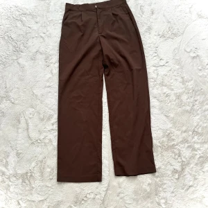 Bruna kostymbyxor - Snygga bruna kostymbyxor med hög midja och rak passform. Perfekta för en stilren look. Byxorna har en diskret dragkedja framtill.