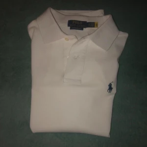 Vit pikétröja från Ralph Lauren - Säljer en klassisk vit pikétröja från Ralph Lauren i custom slim fit. Tröjan har korta ärmar och den ikoniska broderade logotypen på bröstet. Perfekt för en stilren look.