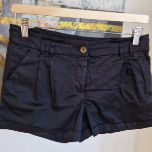 Svarta shorts från H&M - Snygga svarta shorts från H&M med knapp och dragkedja framtill. De har en klassisk design med fickor både fram och bak. Perfekta för en stilren look.