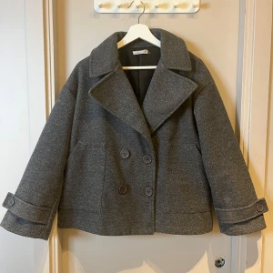 Grå Design by Si kappa - Säljer denna väldigt fina och stilrena kappa, då den tyvärr inte kommit till  användning. Den är lite nopprig vid underarmarna, men annars i väldigt bra skick🥰