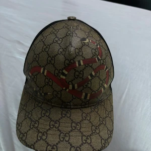 Gucci King Snake keps Beige - Stilig keps från gucci. Kvaliten på denna kepsen är bra färgen är lite sliten annars finns det inga skador på den. Kvitto saknas men den är 100% äkta. Priset är inte hugget i sten
