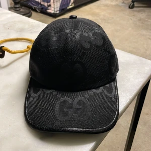 Gucci keps  - Snygg svart keps från gucci med diskret mönster. Perfekt för en stilren look. Justerbar passform för optimal komfort. Kan gå ner i pris vid snabb affär