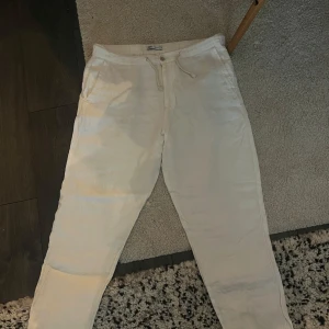 Vita linnebyxor från Zara - Säljer ett par vita linnebyxor från Zara med snörning i midjan. Byxorna har en avslappnad passform och är perfekta för varma dagar. De har fickor fram och bak för extra funktionalitet. Passar för dem med XL i byxor! L för lite mer baggy passform.