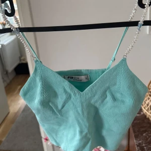 Turkos topp med axelband av pärlor - Snygg turkos ribbad linnetopp från new yorker med smala axelband dekorerade med pärlor. Perfekt för varma sommardagar eller som ett lager under en jacka. Toppen har en enkel och stilren design.