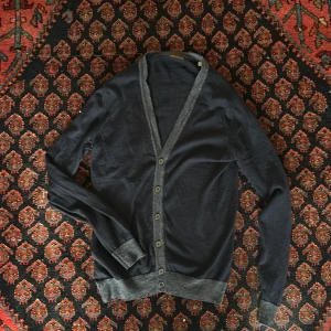 Mörkblå kofta från Stenströms - Säljer en elegant mörkblå kofta från Stenströms med gråa detaljer. Koftan har knappar framtill och långa ärmar. Perfekt för en stilren look.