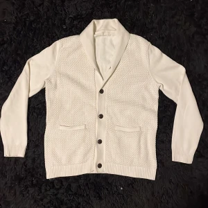 Cardigan  - Snygg vit cardigan med knappar framtill och ribbade muddar. Den har en texturerad framsida och två fickor. Perfekt för lager-på-lager ny till våren och sommaren. Hör va dig om du har några funderingar 