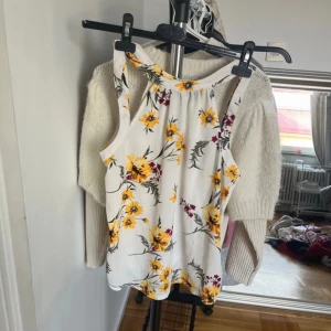 Blommig ärmlös topp - Säljer en vit ärmlös topp med ett färgglatt blommönster i gult och rött. Perfekt för sommardagar och kan enkelt matchas med jeans eller kjol.