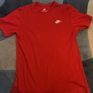 Röd t-shirt från Nike - Säljer en klassisk röd t-shirt från Nike med korta ärmar och det ikoniska Nike-loggan i vitt på bröstet. Perfekt för en sportig look eller avslappnad stil. Passar bra till både träning och vardag.