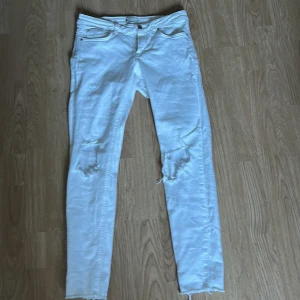 Vita jeans från G Perfect Jeans - Snygga vita jeans från G Perfect Jeans med slitna detaljer på knäna. De har en tight passform och är perfekta för en trendig look. Byxorna har en dragkedja och knapp framtill.