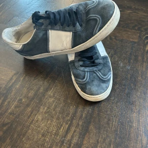 Valentino Flycrews i blå mocka - Snygga sneakers från Valentino Garavani i grå mocka med vita detaljer. Skorna har svarta snören och en rund tå. Perfekta för en stilren look med en touch av lyx, som är äkta.