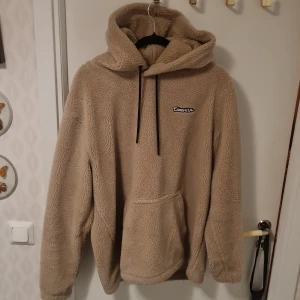 Beige fleece hoodie från H&M - Mysig beige hoodie från H&M i fleece-material. Perfekt för kyliga dagar med sin varma och mjuka känsla. Den har en stor huva och en praktisk magficka framtill. Svarta dragsnören vid huvan ger en snygg kontrast. Perfekt för en avslappnad stil.