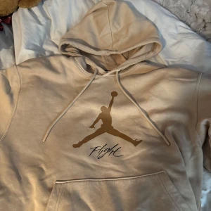 Beige hoodie från Jordan - Säljer en snygg beige hoodie från Jordan med det ikoniska Jumpman-logotypen och texten 'Flight' på framsidan. Hoodien har en stor ficka framtill och justerbar huva med dragsko. Storlek M 