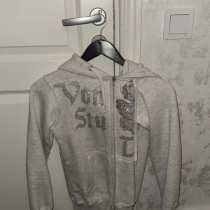 Grå hoodie från Vonstudio - Säljer en snygg grå hoodie från Vonstudio med glittriga detaljer och dragkedja framtill. Perfekt för en casual look med stil. Den har en bekväm passform och är idealisk för kyligare dagar.