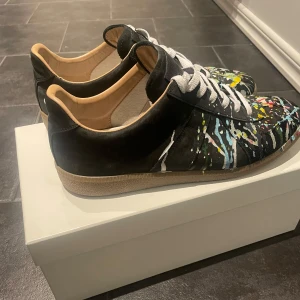 Maison Margiela skor - Unika svarta sneakers från Maison Margiela med coola färgstänk i blått, gult och vitt. Skorna har en klassisk snörning och en bekväm gummisula. Perfekta för dig som vill sticka ut med stil. Skick 8/10✅  Skriv vid frågor eller funderingar i DM🍾