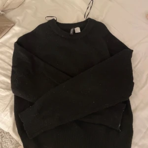 Svart tröja från H&M - Säljer en stilren svart tröja från H&M. Tröjan har en klassisk rund halsringning och långa ärmar. Perfekt för kyligare dagar och enkel att matcha med olika outfits. Passar både till vardag och mer uppklädda tillfällen.