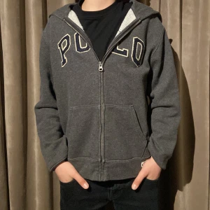 Ralph Lauren zip - Säljer en grå hoodie med dragkedja från Polo. Den har en stor broderad logga på framsidan och en bekväm huva. Perfekt för en avslappnad stil. Modellen är 155 och väger 45 så passar någon 155-165 bäst. Vårt pris endast 129, men inte hugget i sten. Kom med minsta fråga😊