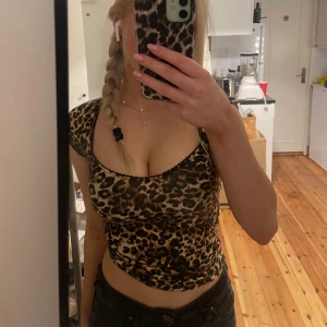 Leopardmönstrad topp från Nelly - Säljer en snygg, trendig leopardmönstrad topp från Nelly. Toppen har korta ärmar och en v-ringad design med svarta spetsdetaljer längs kanten. (lite stor i storleken)