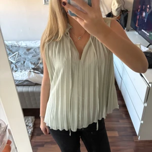 Vit ärmlös blus - Säljer en stilren vit ärmlös blus med plisserad design. Blusen har en lös passform och en diskret knytning vid halsen. Perfekt för en elegant och luftig look💕
